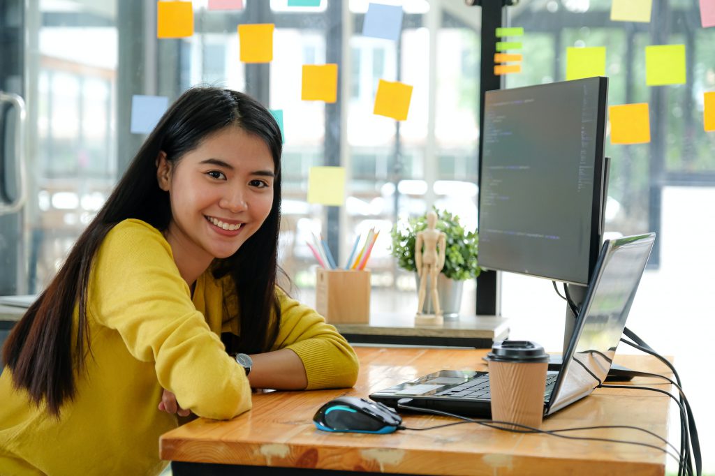 Asian female programmer sat at her desk at the office. She looked and smiled happily.